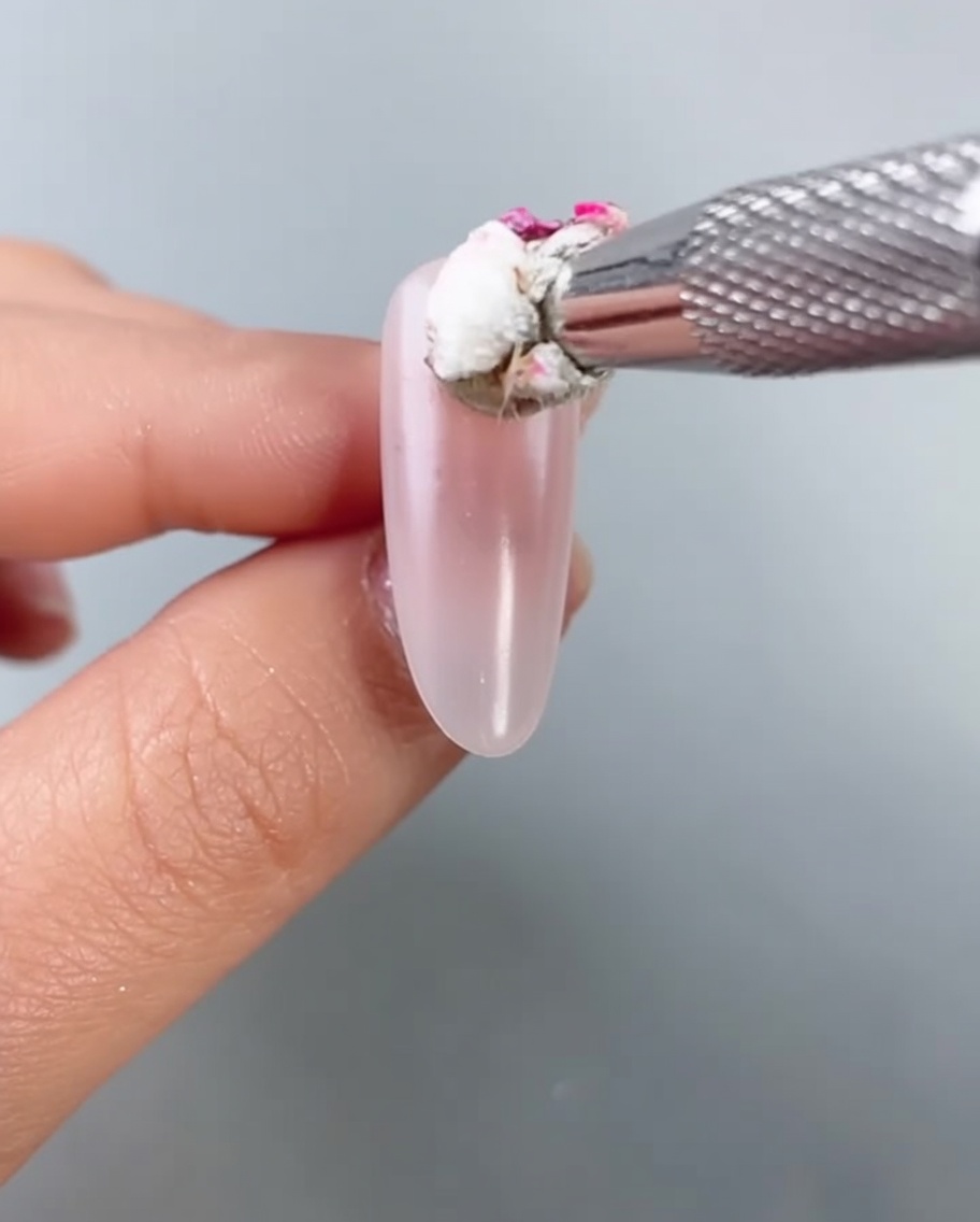 Primo piano di una spugnetta che tampona del gel rosa acceso al centro di ununghia a mandorla per creare un effetto sfumato.