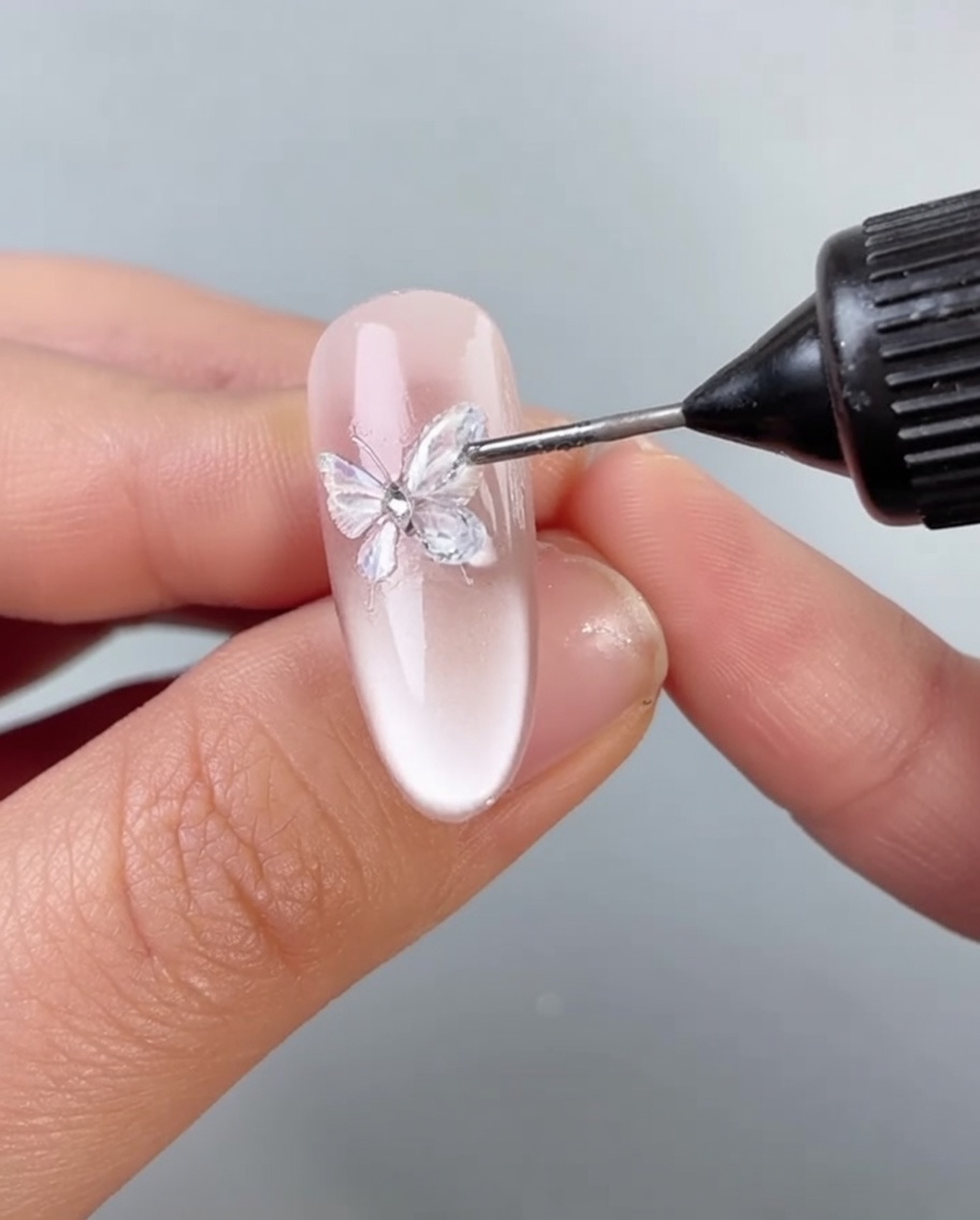 Un pennellino applica uno strato sottile di gel trasparente attorno alla base di una decorazione a farfalla su ununghia.