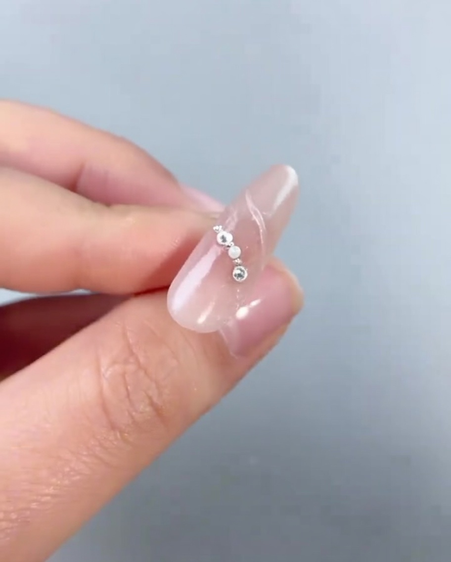 Primo piano di un ciondolo a forma di stella argentata che viene posizionato su ununghia decorata con piccole perle e microsfere.
