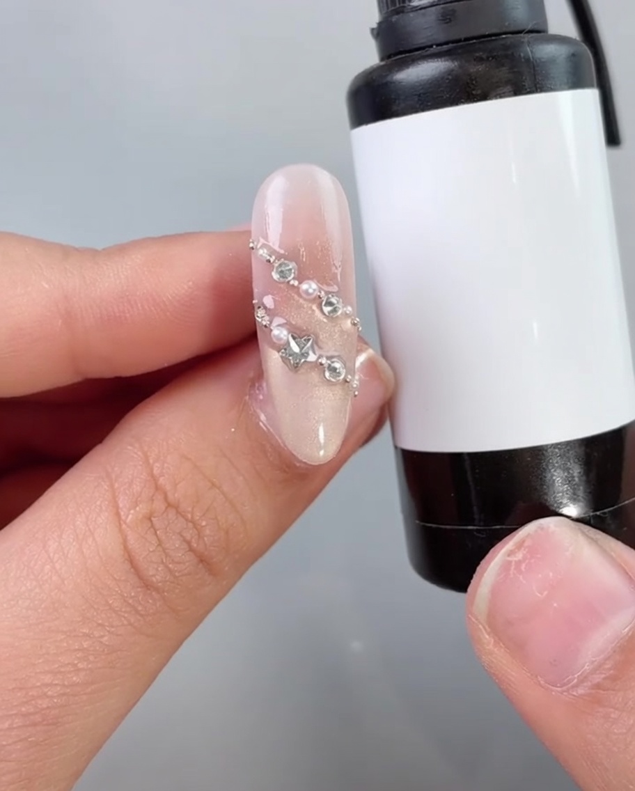 Un pennello per unghie applica un top coat trasparente o un sigillante su ununghia decorata con perle e strass.