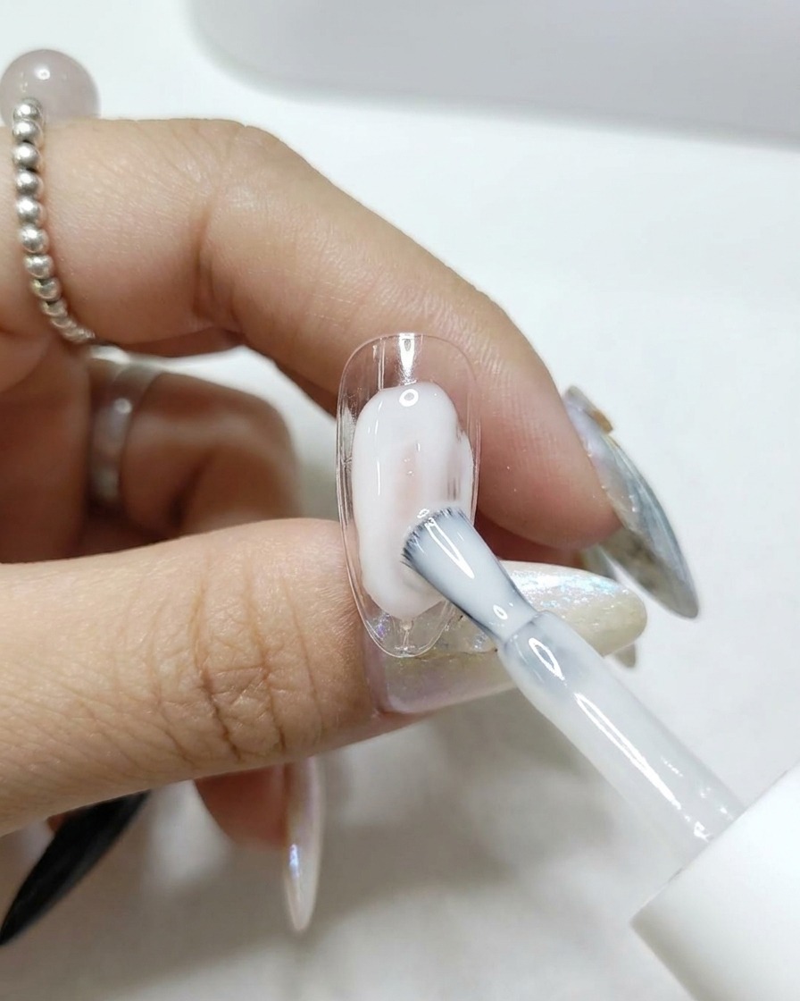 Un pennello che applica un top coat trasparente e lucido su una tip per unghie.