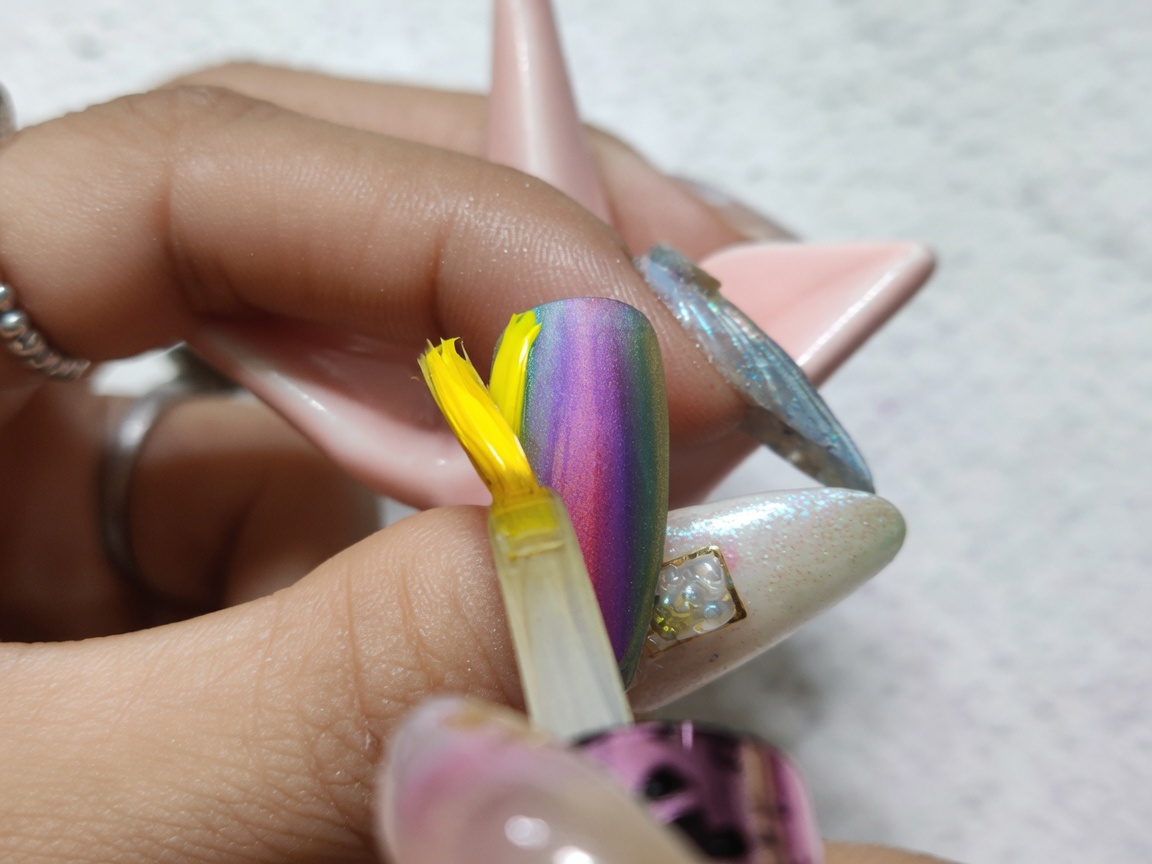 Un pennello che stende un top coat trasparente e lucido su ununghia completata con un vivace gradiente ad acquerello.