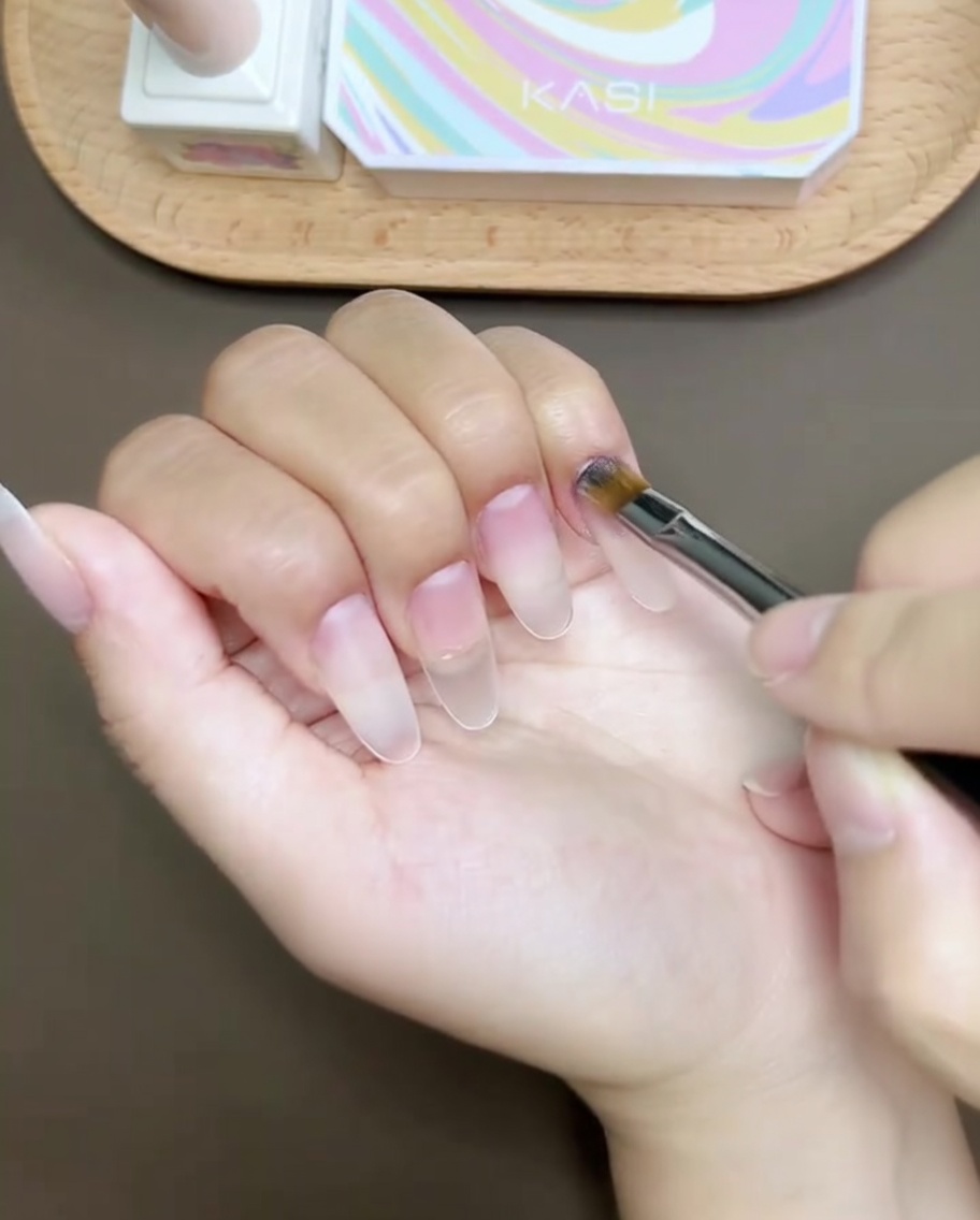 Un pennello applica un gel strutturale trasparente sulla superficie preparata dellunghia, creando una finitura liscia e livellata.