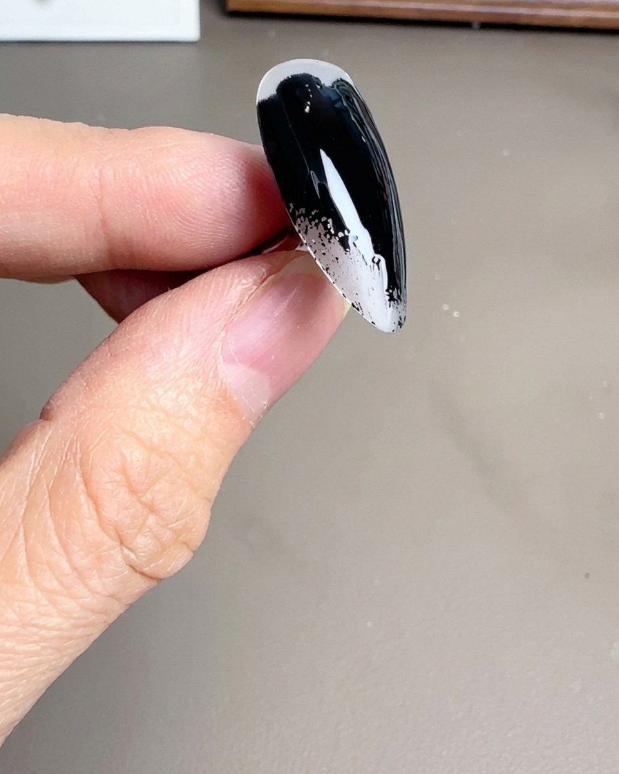Primo piano di un pennello che applica uno smalto gel nero lucido su una tip trasparente a forma di stiletto.
