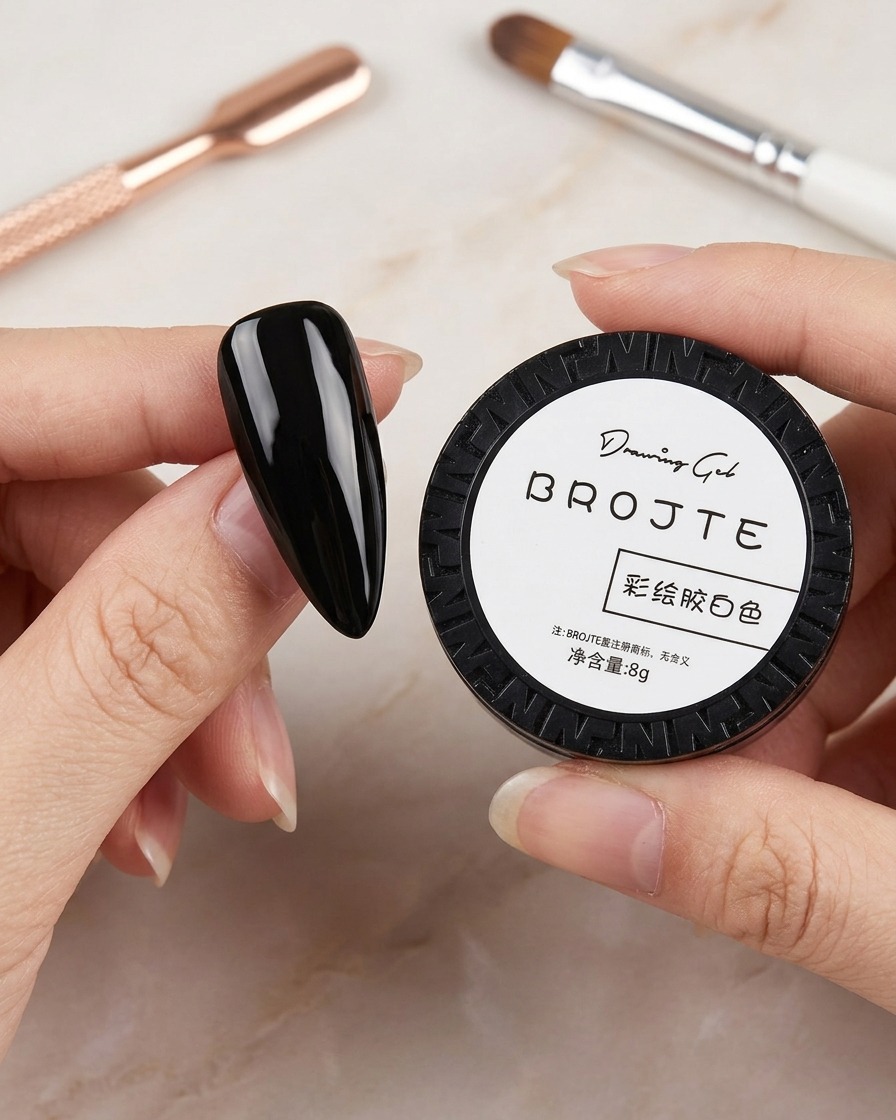 Una mano che tiene un piccolo vasetto nero di gel per micropittura bianco, con pennelli per nail art visibili sullo sfondo sfocato.