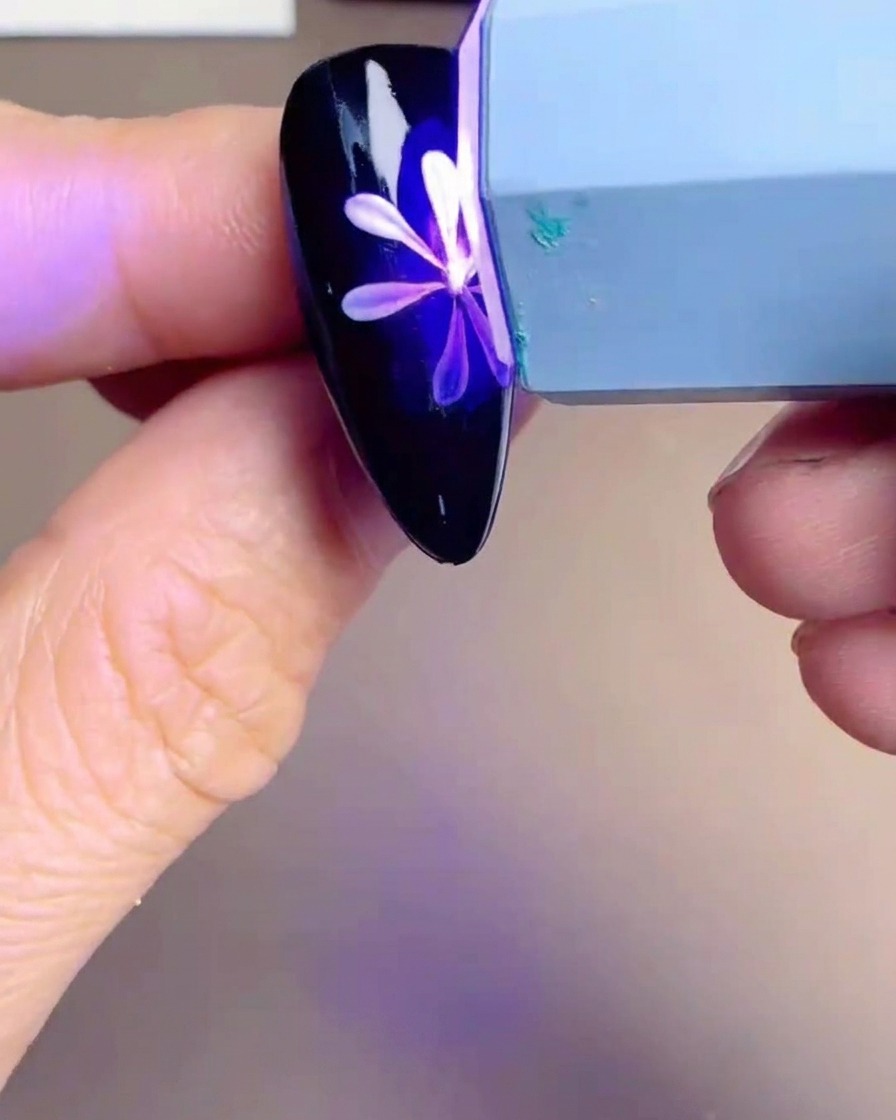 Una lampada UV/LED portatile posizionata sopra una tip con un design a margherita bianca e gialla, che emette una luce viola.