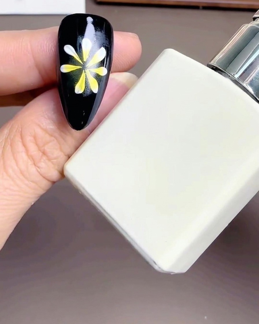 Primo piano di una bottiglietta rettangolare bianca di Diamond Top Coat tenuta vicino a ununghia decorata con un fiore.