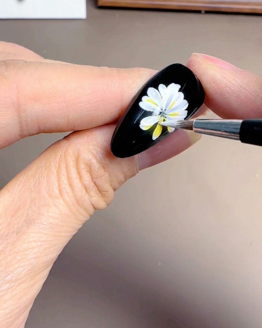 Primo piano di una mano che aggiunge petali bianchi sovrapposti a un design a margherita su uno sfondo nero.