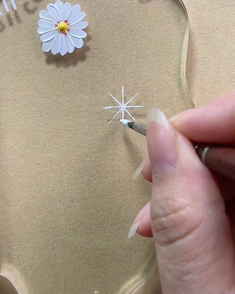 Un primo piano che mostra un pennello mentre aggiunge gel bianco per ispessire una linea diagonale, trasformandola in un petalo arrotondato a goccia.
