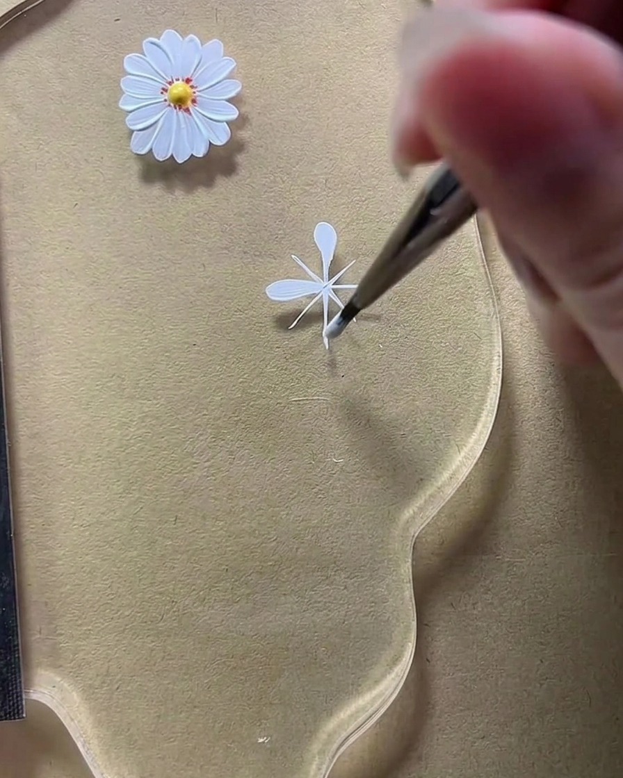 Primo piano del pennello da nail art mentre modella un secondo petalo arrotondato sulla linea di guida diagonale inferiore sinistra.