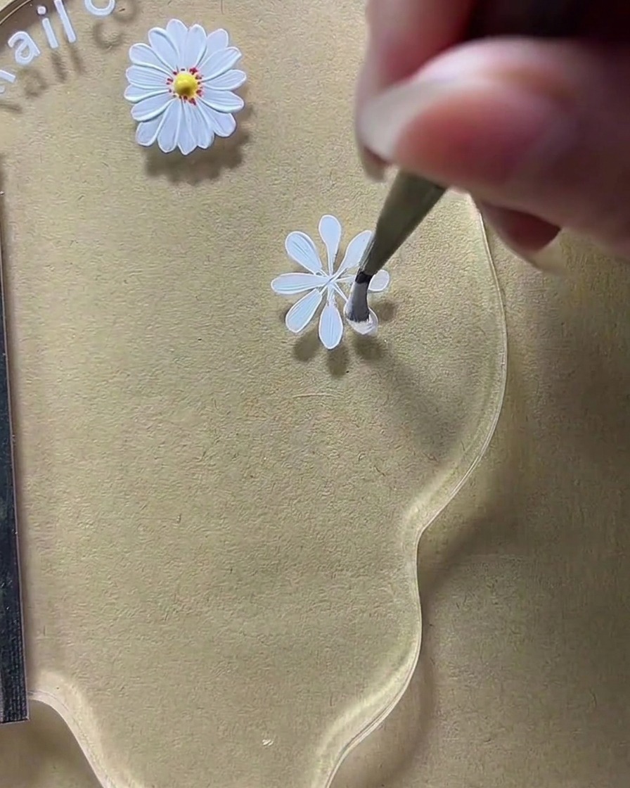 Primo piano di una tavolozza per nail art in cui un pennello sta allargando le forme dei petali bianchi sui lati orizzontali.