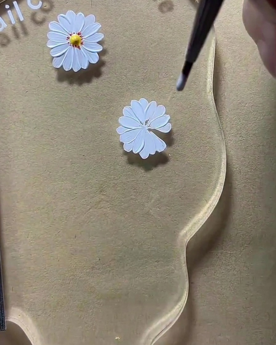 Un dotter da nail art che deposita un punto di gel giallo al centro del disegno della margherita bianca.