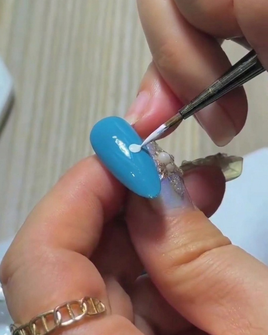 Dettaglio della punta di un pennello liner immersa in una piccola quantità di smalto gel bianco su una tavolozza.