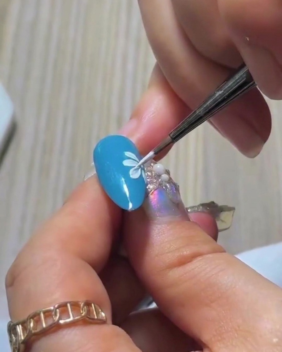 Uno scatto ravvicinato del quarto petalo bianco dipinto sullunghia blu, costruendo la fila iniziale del design a margherita.