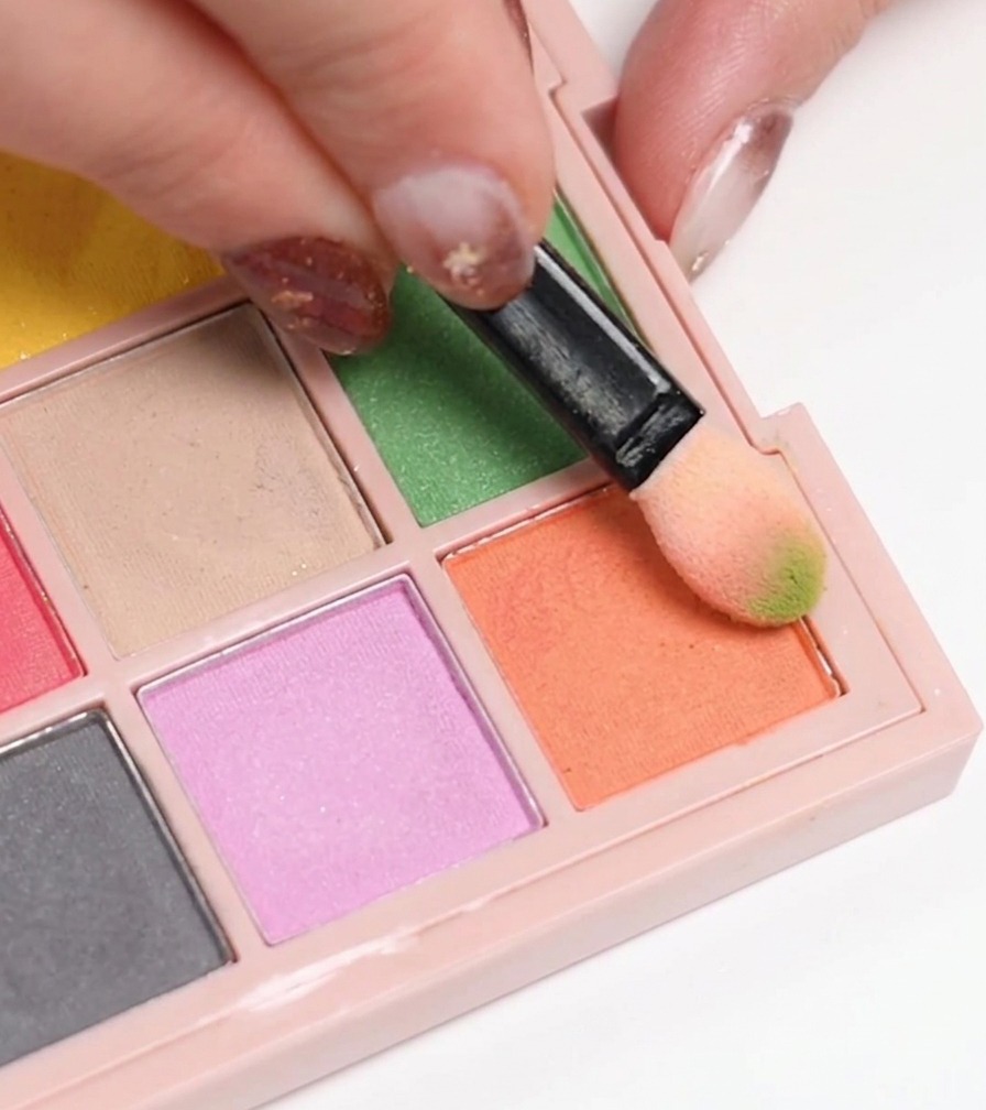 Una spugnetta per trucco che preleva smalto gel arancio da una tavolozza per applicarlo su ununghia.