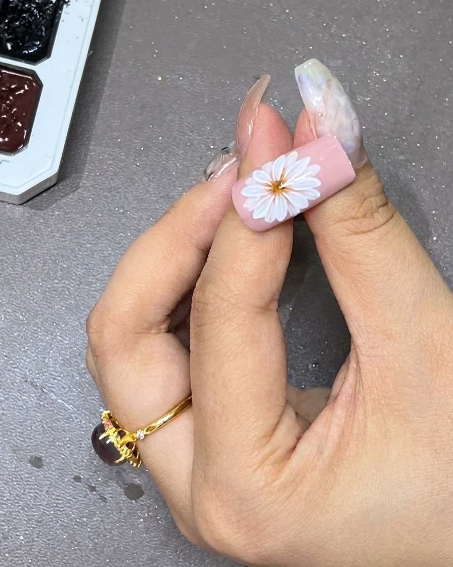 Un punto di gel nero posizionato con cura al centro del fiore bianco a strati sullunghia.