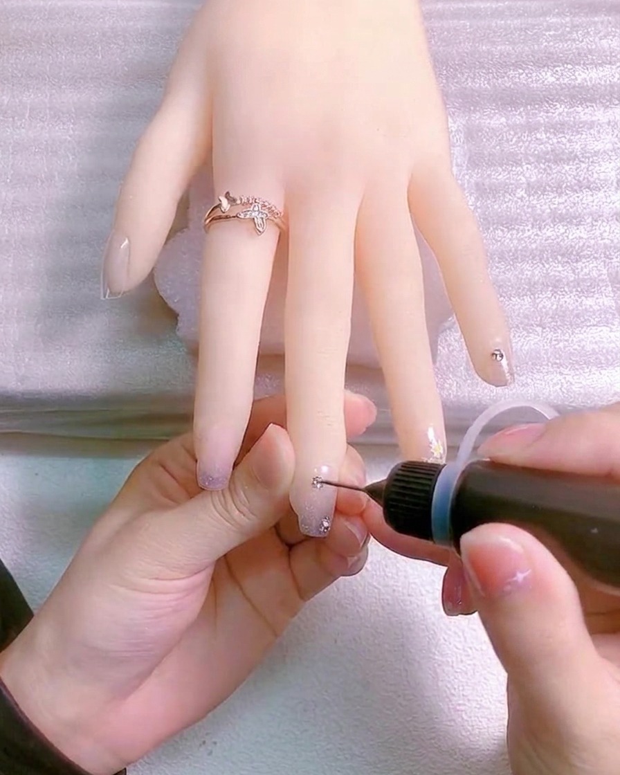 Un pennello fine applica gel trasparente intorno alla base di un charm di cristallo.