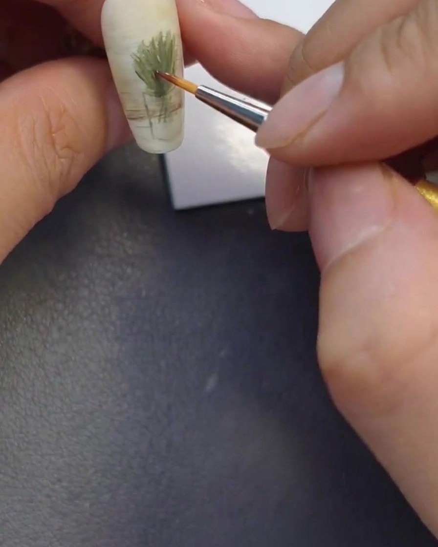 Primo piano di un pennello sottile che applica piccoli punti di marrone, arancione e giallo sullunghia per formare i centri dei fiori.