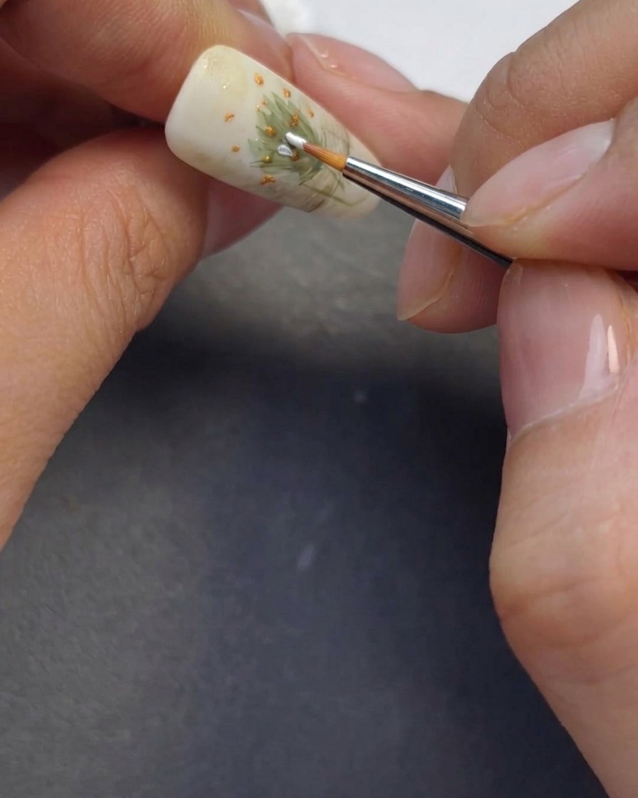 Un pennello sottile che dipinge delicati petali di margherita bianchi attorno ai centri dei fiori precedentemente creati.