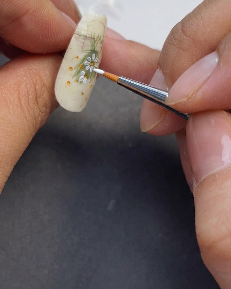 Primo piano di altri petali bianchi dipinti sullunghia per completare il design della margherita.
