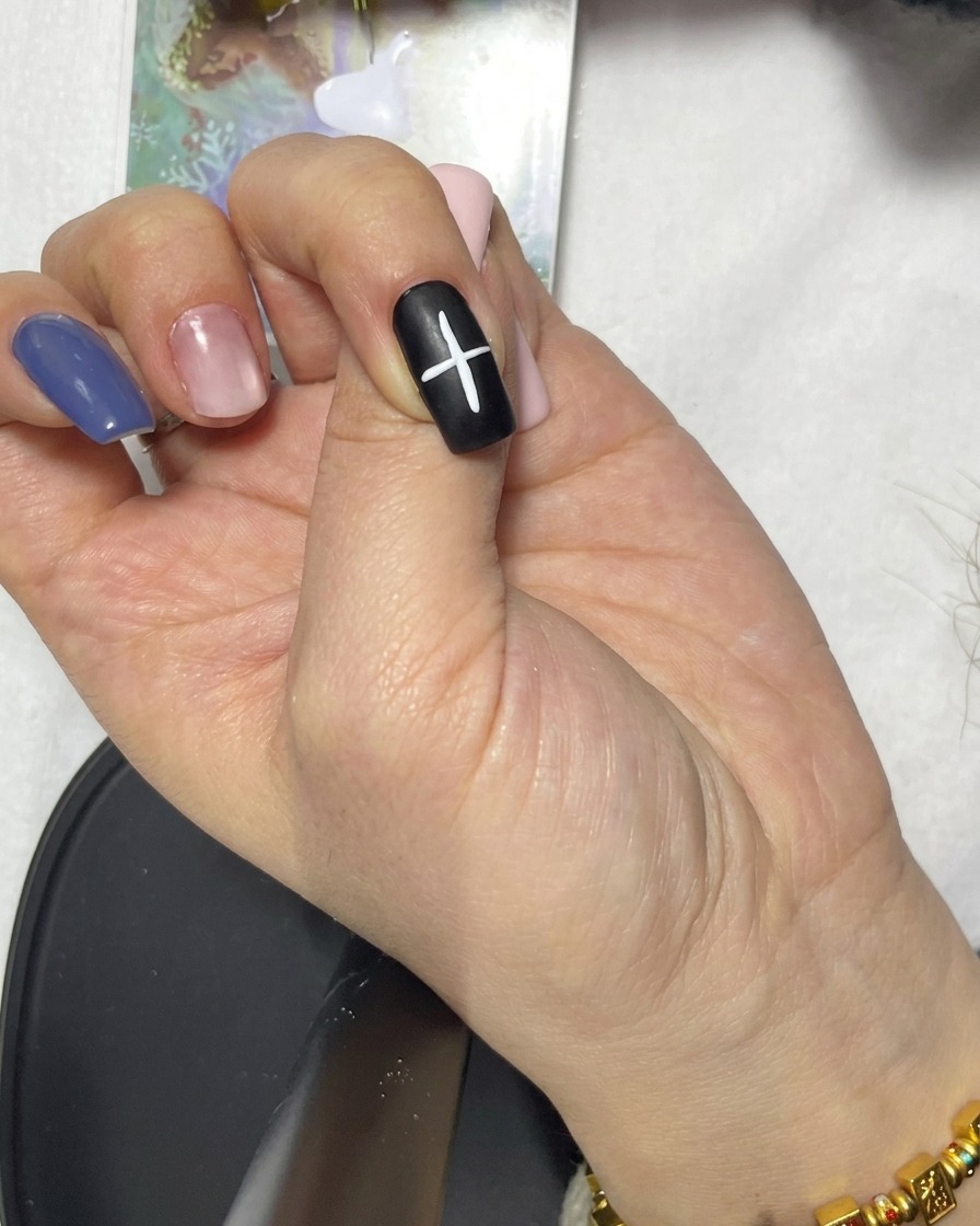 Un primo piano di una linea bianca diagonale aggiunta alla forma a croce esistente su ununghia nera.