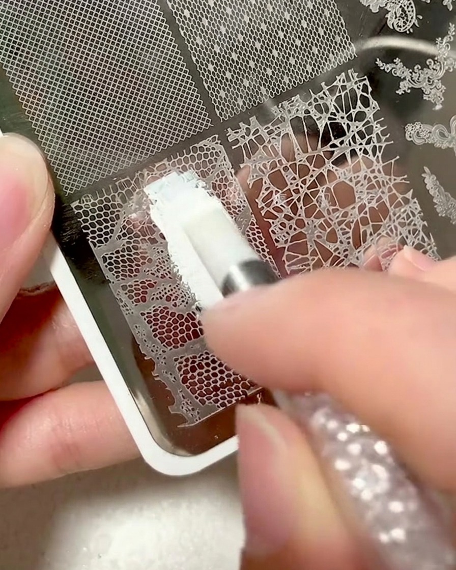 Primo piano di una piastra metallica con design in pizzo coperta da gel bianco per stamping.