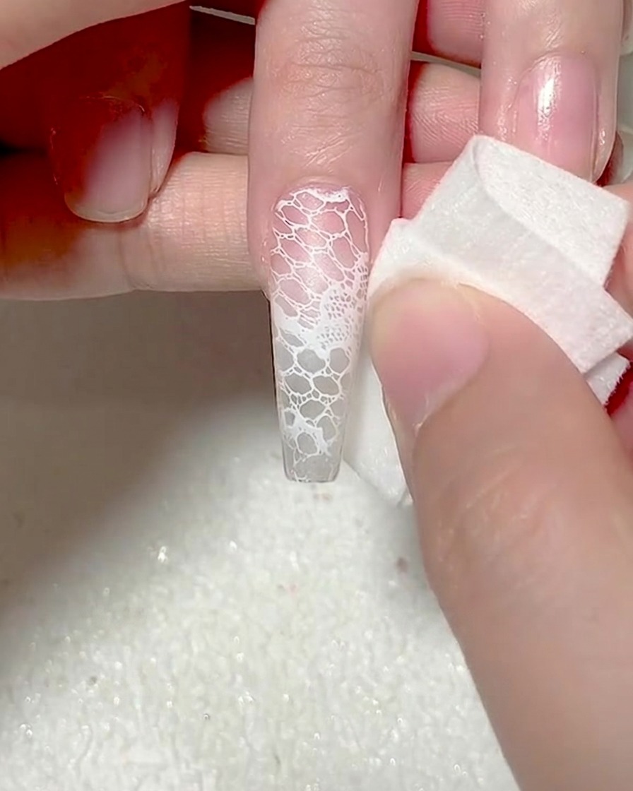 Primo piano di una spugnetta per trucco che tampona gel bianco sulla punta dellunghia per un effetto ombre.