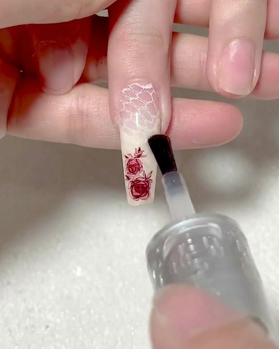 Un pennello applica gel base trasparente sopra lo sticker della rosa per incapsularlo.