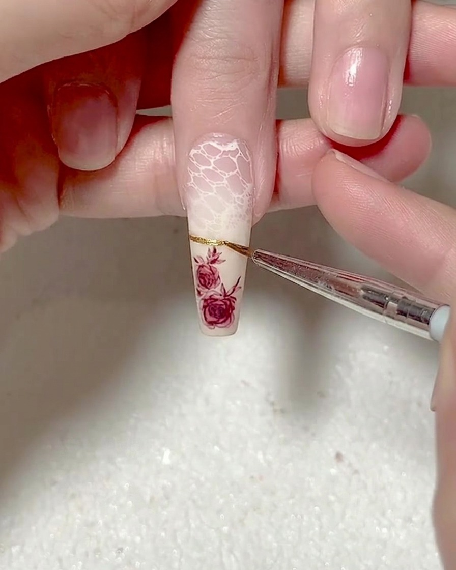 Primo piano di un pennello liner che traccia una linea sottile e precisa con gel metallizzato dorato sulla punta dellunghia.