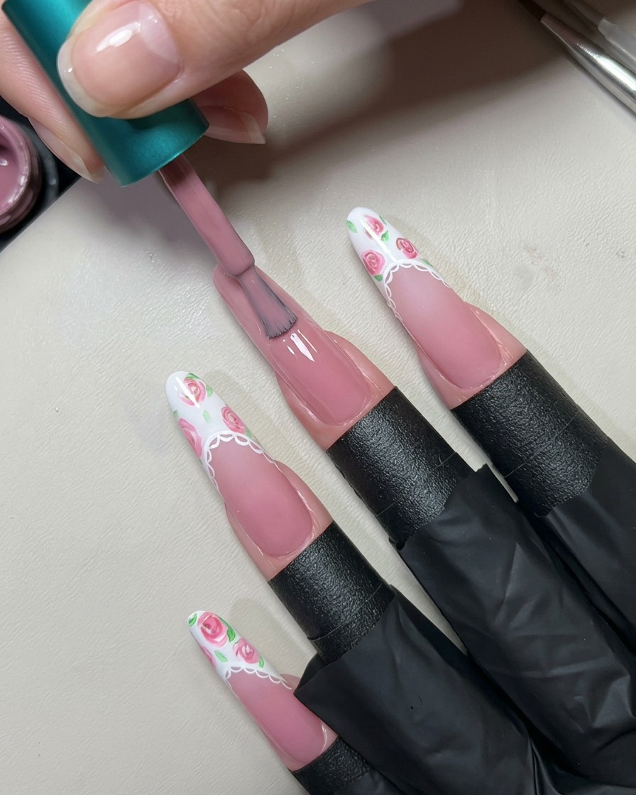 Un pennello applica uno strato di gel nude rosato traslucido su ununghia lunga preparata.