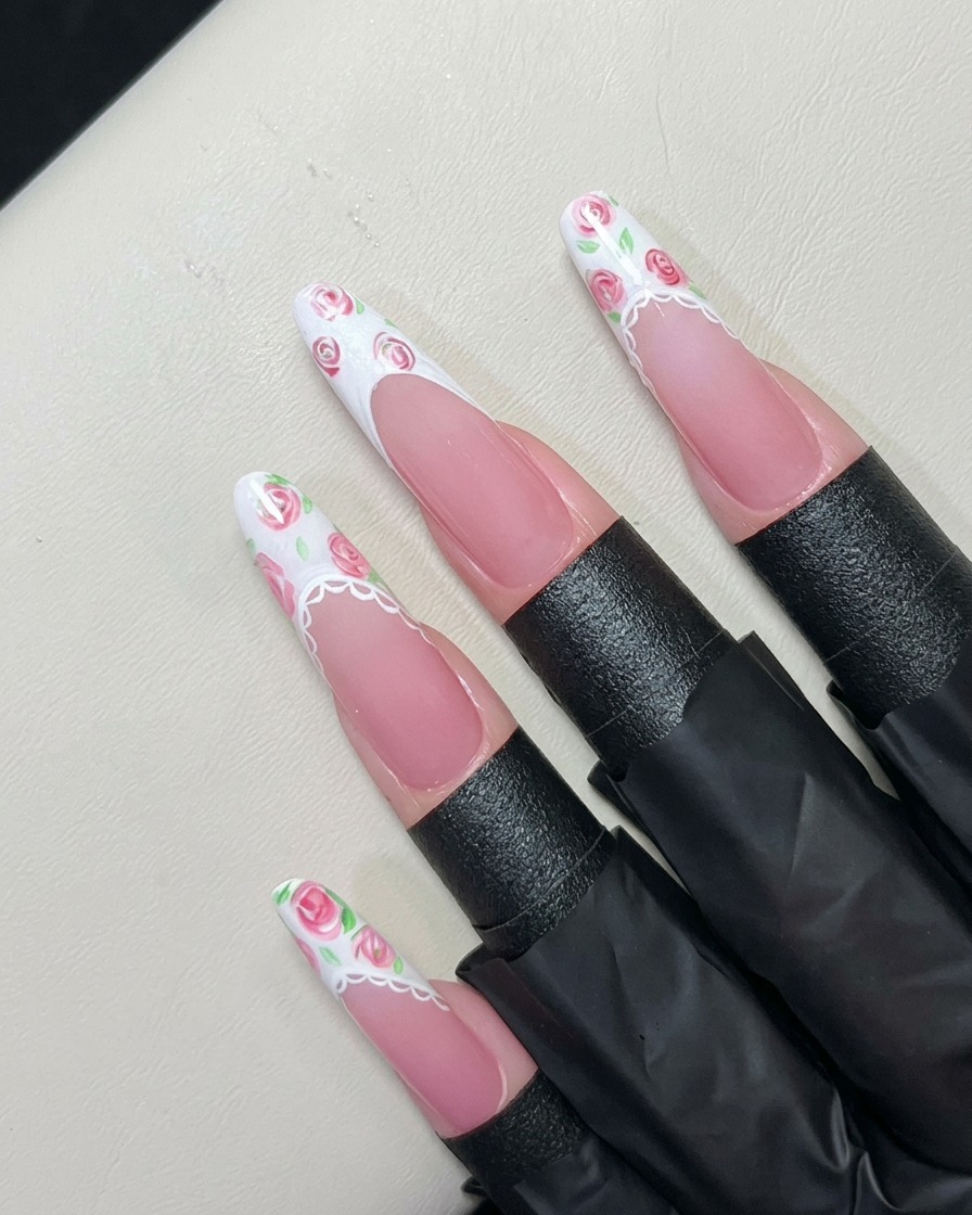 Un pennello liner dipinge minuscole foglie verdi attorno alle rose rosa sulla punta bianca.