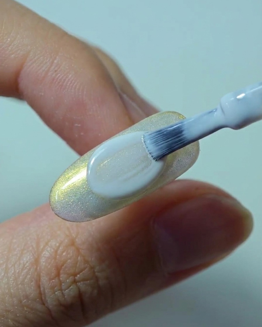 Un pennello applica un secondo strato liscio e coprente di smalto gel bianco sopra lunghia.