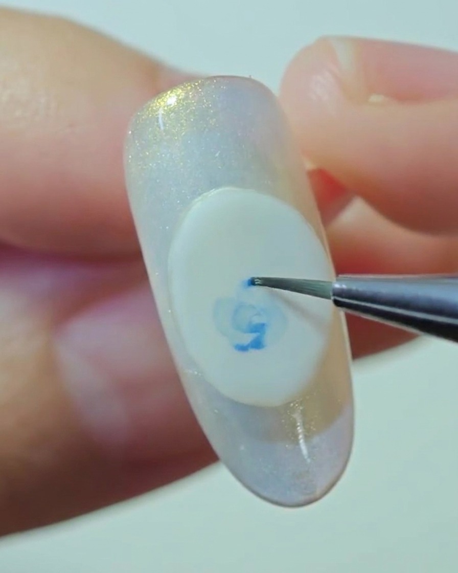 Una vista ravvicinata di un pennello di precisione che sfuma delicatamente i bordi di una rosa blu dipinta su una base in gel bianco.