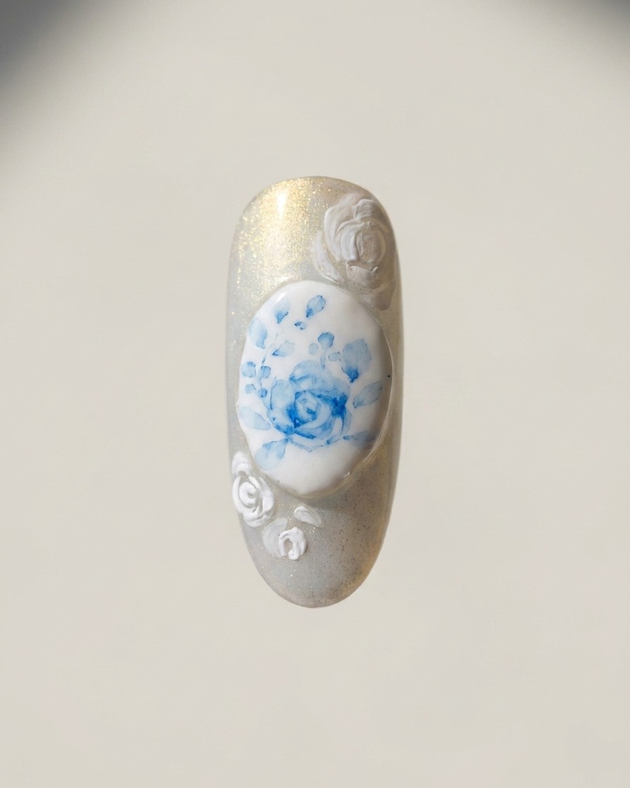 Un pennello a punta sottile dipinge contorni di rose bianche sui bordi dellunghia attorno al design della rosa blu centrale.