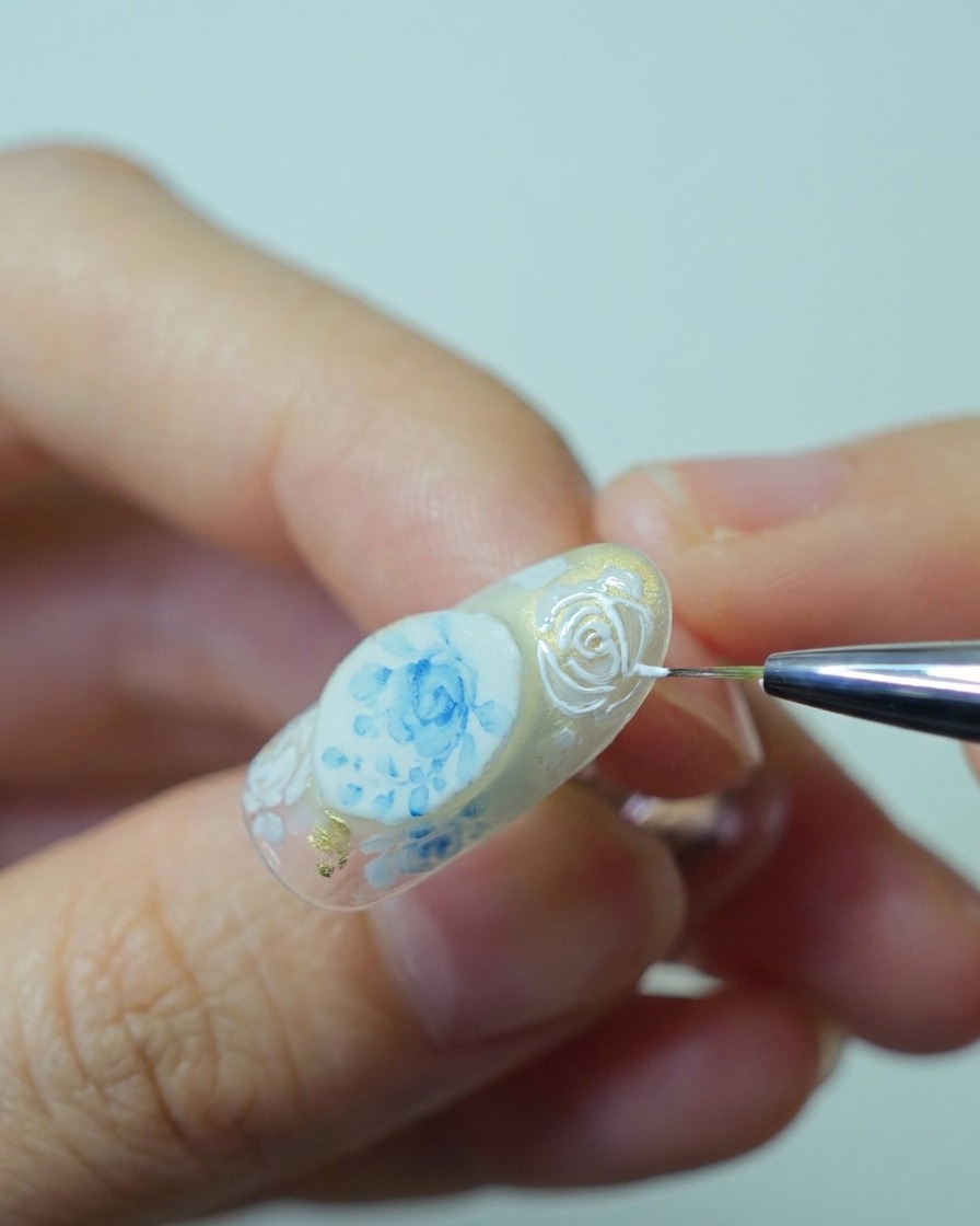 Primo piano di un pennello che applica uno spesso gel bianco in rilievo sopra i contorni delle rose precedentemente dipinti per creare una texture 3D.