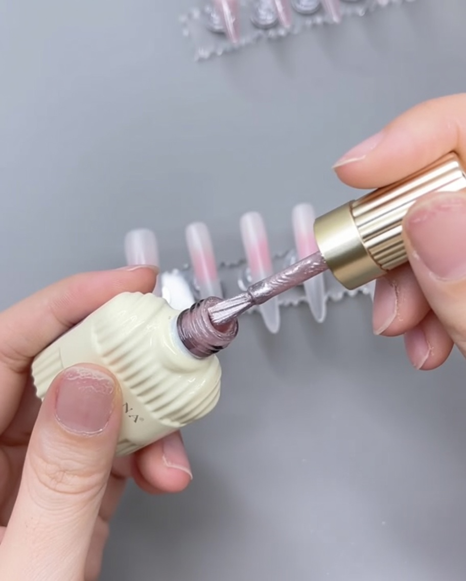 Un pennello applica gel cat-eye rosa sopra una base rosa polimerizzata su una tip.