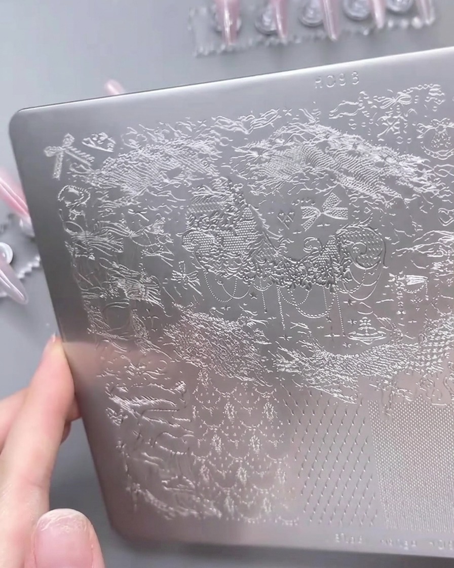 Vista ravvicinata di una piastra per stamping metallica con gel bianco distribuito su un motivo in pizzo.