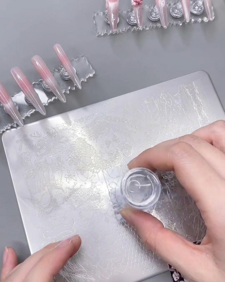 Uno stampino in silicone trasparente preme su una piastra metallica, sollevando il design in pizzo.