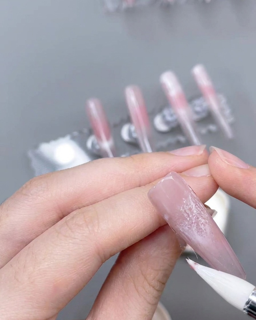 Un pennello a punta sottile crea precise linee daccento rosa su ununghia decorata.