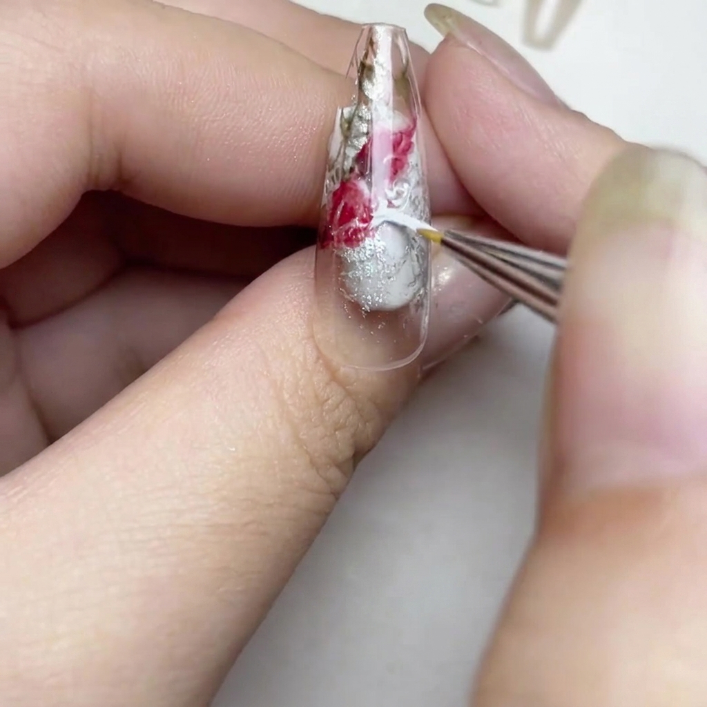 Primo piano di ununghia che mostra un pennello che aggiunge pennellate sottili di vernice bianca per creare un effetto rosa ad acquerello negli spazi vuoti.