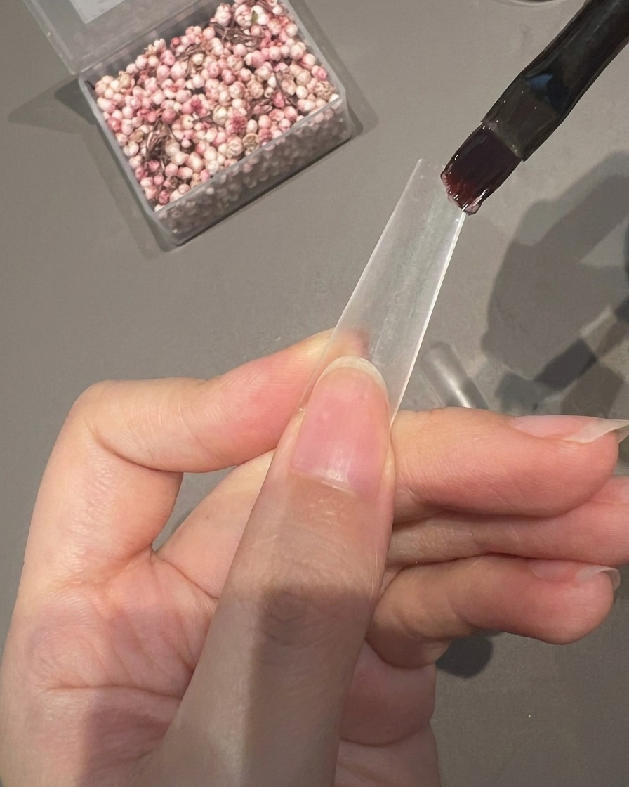 Un pennello applica uno strato di gel adesivo trasparente sulla metà inferiore di una tip per unghie.