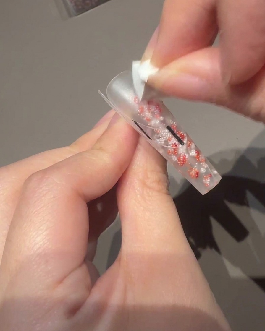 Uso di un piccolo pennello per gel per applicare uno smalto rosa lattiginoso sullunghia.