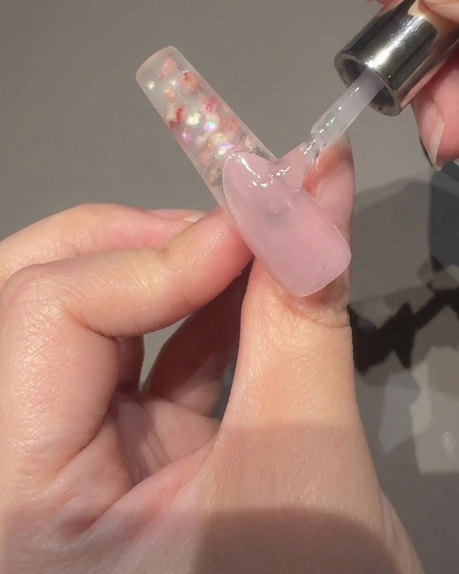 Una mano che tiene un magnete cilindrico accanto a ununghia con gel cat-eye umido, mostrando il riflesso che si sposta al centro.