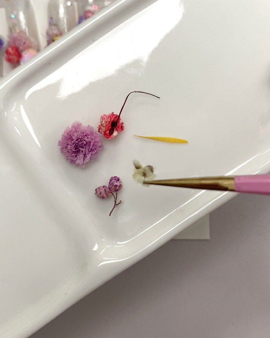 Una vista ravvicinata di un paio di pinzette che tengono una rosa secca mentre ne tagliano la base dello stelo.