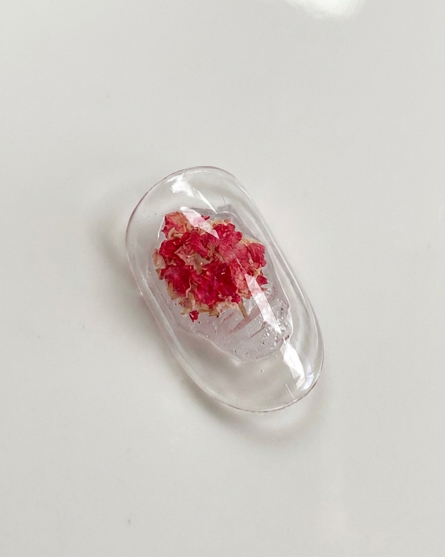 Un pennello a punta sottile che preme delicatamente sui petali di una rosa secca incorporata nel gel dellunghia.