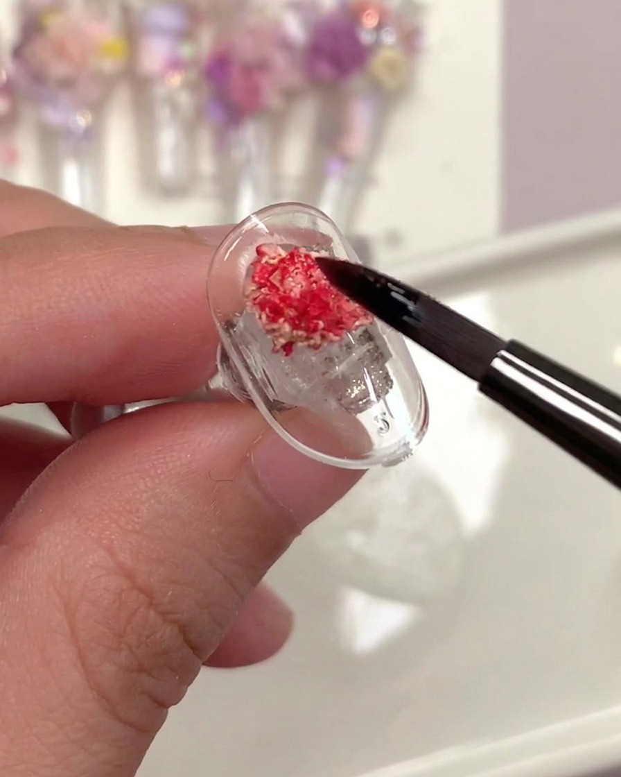Un pennello che applica un top coat trasparente sopra una rosa secca su ununghia.
