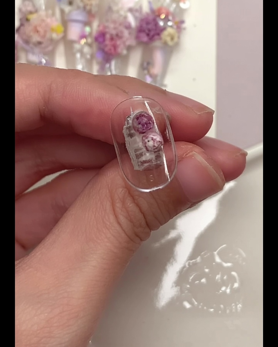 Un pennello a punta sottile che preme delicatamente sui fiori sferici viola posizionati su una tip trasparente.