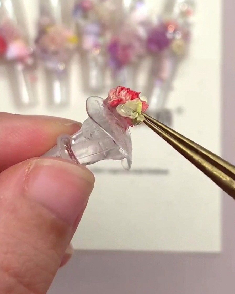 Una mano che usa le pinzette per posizionare una testa di fiore a tromba su una tip decorata con altri fiori.