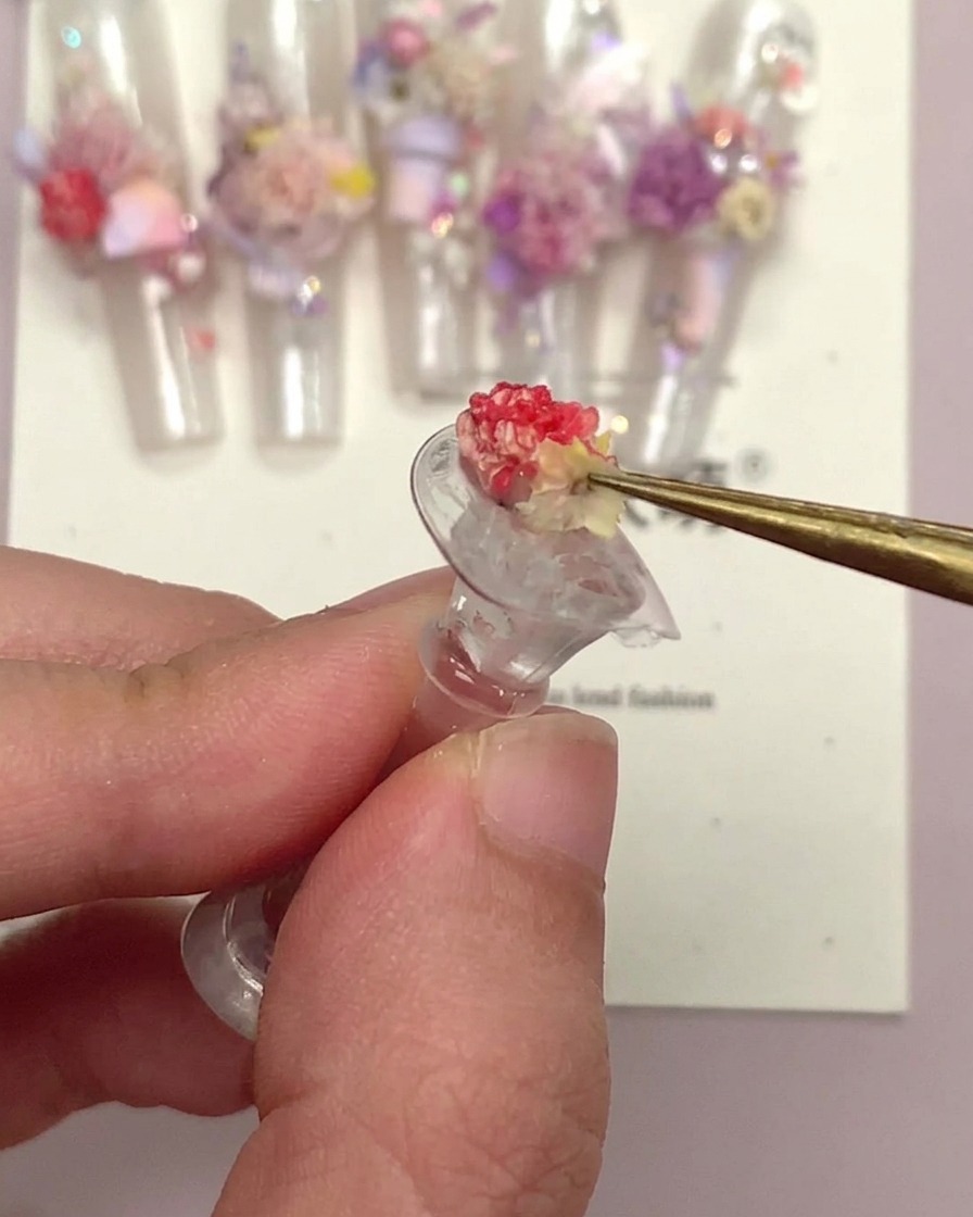 Un paio di pinzette che tengono un piccolo ornamento floreale per unghie dopo che è stato incapsulato.