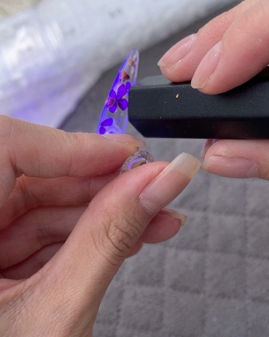 Una mano tiene una lampada UV/LED portatile sopra una tip decorata con fiori e strass.